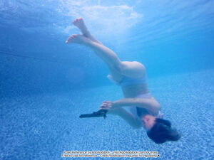 thin white female model in an upsidedown underwater pose with a revolver