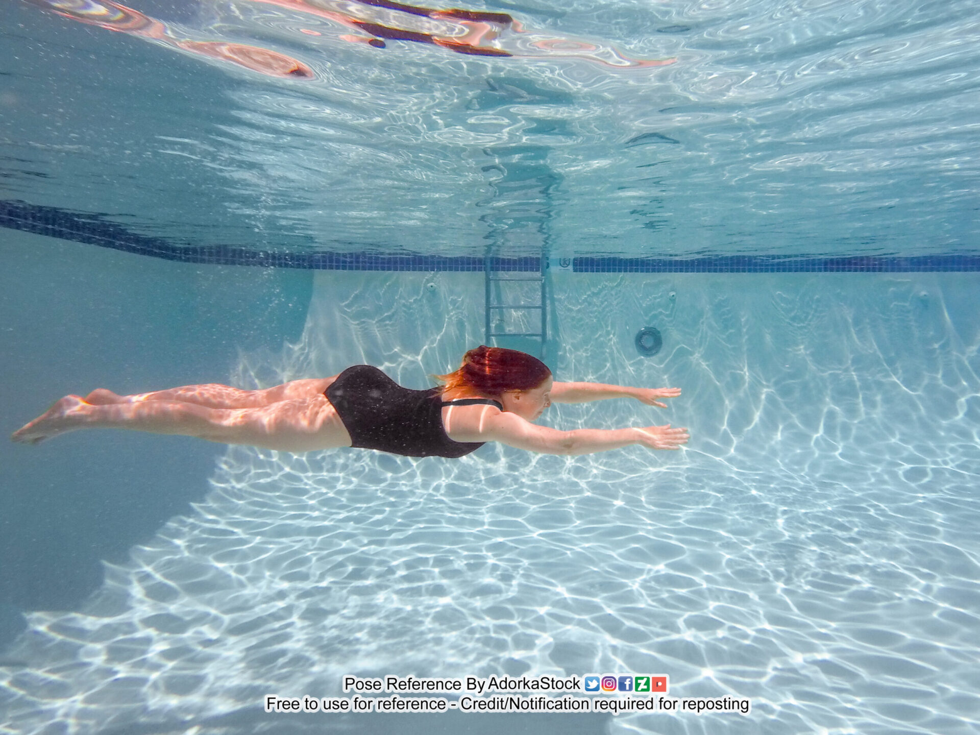thin white female model swimming underwater horizontally, arms outstretched as if flying