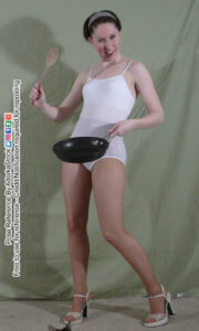 A white woman in a white leotard wearing heels, holding a spoon and a frying pan, smiling.