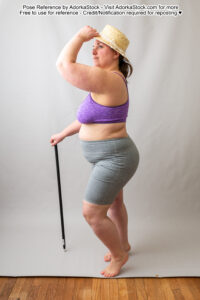 fat white female model standing in profile holding a cane and touching the rim of her hat